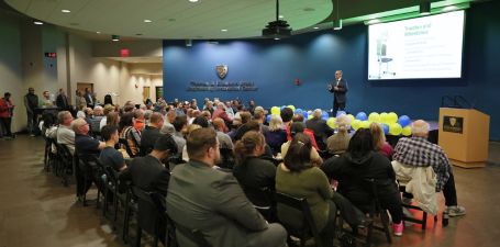 Tech419 Pitch Competition Man in a suit standing on a stage speaking in front of a room full of people at the University of Toledo Business Incubator's Tech419 Pitch Competition.